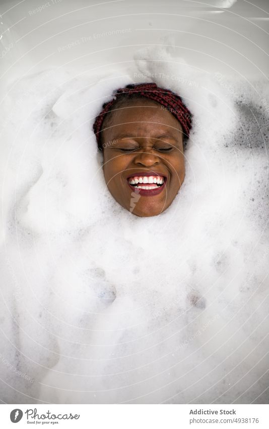 Glückliche Afroamerikanerin im schäumenden Wasser Frau Badewanne Seife Lachen Spa Wochenende Hautpflege jung schwarz ethnisch heiter Hygiene Wellness