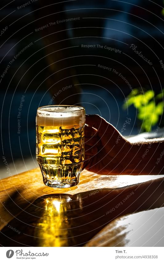 ein Pilsener Bierglas in einer Hand glass Glas Licht Alkohol Biergarten Prenzlauer Berg Berlin Menschenleer Außenaufnahme Farbfoto Getränk Stadt trinken Tag