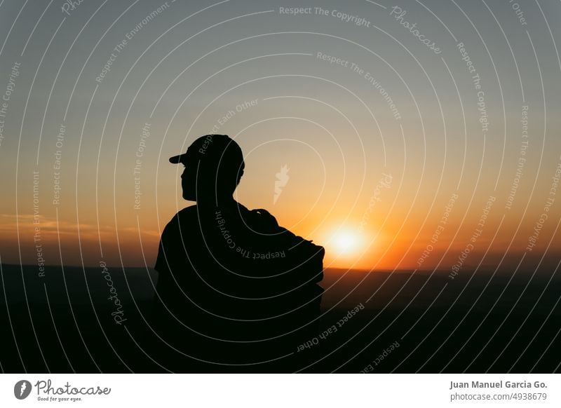 Silhouette eines Mannes mit Mütze und Rucksack, der die Landschaft im orangefarbenen Licht des Sonnenuntergangs betrachtet Therapie Teenager Erfahrungen
