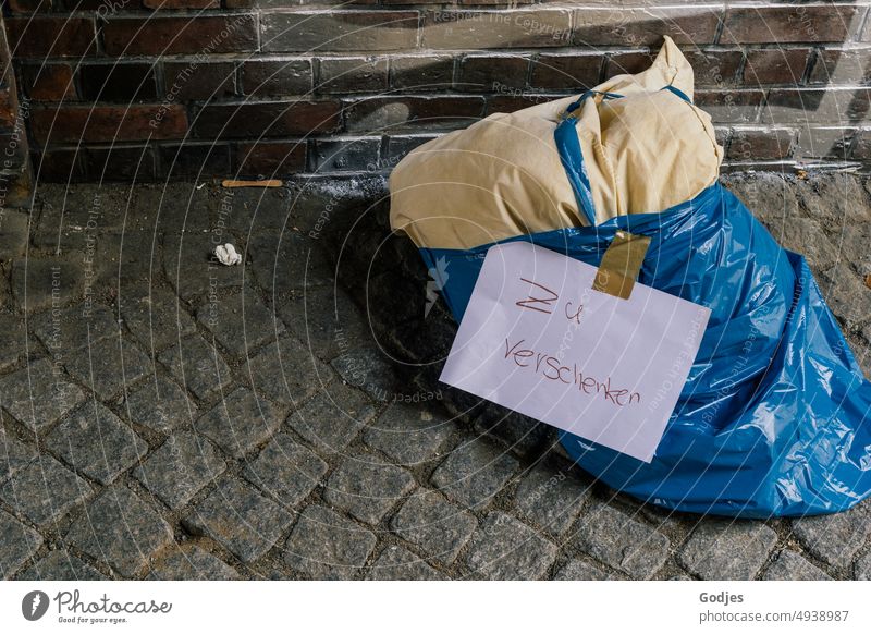 Ein Kissen in einem Müllsack liegt am Straßenrand mit der Aufschrift "zu verschenken Objekte Obdachlosigkeit Geschenk Boden Hintergrund Kontext Hilfsbedürftig