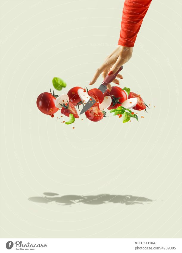 Frauen Hand mit Messer machen Caprese Salat mit auf hellgrünem Hintergrund mit Schatten. Caprese-Salat fliegen Tomate Mozzarella Herstellung Basilikumblätter