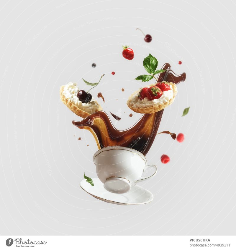 Kreative Levitation Lebensmittel-Konzept mit fliegenden Kaffee Spritzen in Tasse und Kuchen mit verschiedenen Beeren und Früchte auf hellem Hintergrund.