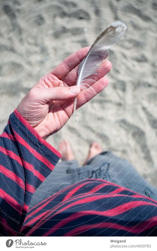 Feder in Handfläche mit Blick nach unten auf den Sandstrand Strand Ostsee Norddeutschland Schleswig-Holstein Urlaub sammeln Achtsamkeit Meer Sonne barfuß Poesie