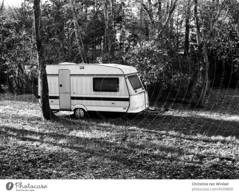 Ein alter Wohnwagen auf einer Wiese mit Bäumen und Sträuchern und langen Schatten Camping Ferien & Urlaub & Reisen Campingplatz Erholung retro Mobilität