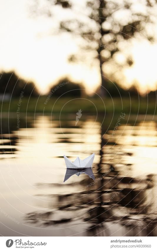 Ein Papierboot schwimmt auf den Wellen im Wasser bei einem schönen Sonnenuntergang. Origami Schiff Segeln. Das Konzept eines Traums, Zukunft, Kindheit, Freiheit oder Hoffnung.