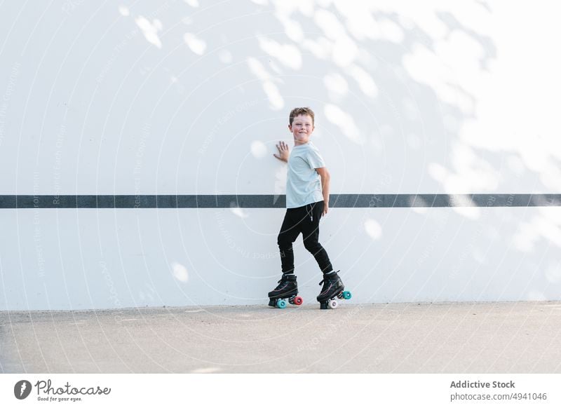 Glücklicher Junge auf Rollschuhen auf der Straße Mitfahrgelegenheit Rollerskate Sommer Wochenende Aktivität Hobby tagsüber Lächeln urban Kind Zeitvertreib