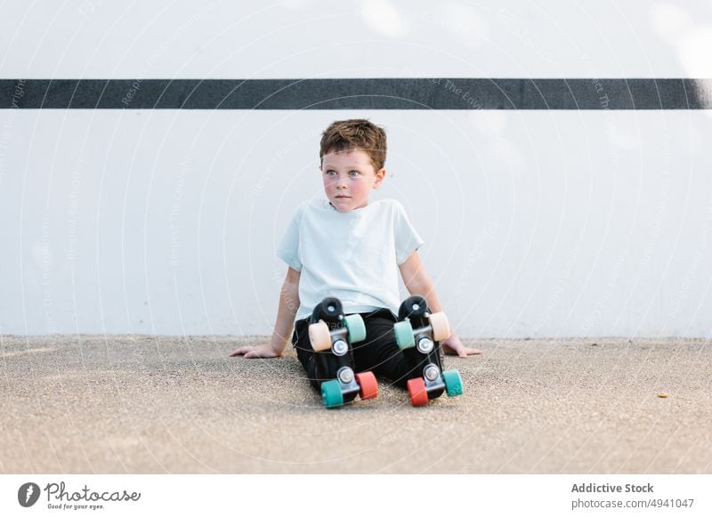 Junge in Rollschuhen auf dem Boden sitzend Rollerskate Pause Straße Wand Hobby Sommer Aktivität Kind lässig ruhen sich[Akk] entspannen tagsüber Kindheit