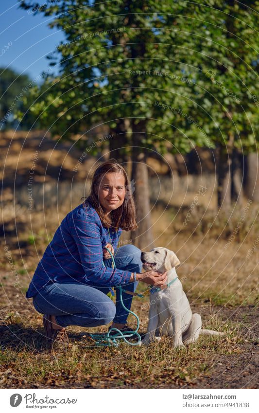 Glückliche brünette Frau mittleren Alters kniet mit ihrem kleinen Labrador-Welpen auf einem ländlichen Weg Retriever Spaziergang Leine ziehen Besitzer Sommer