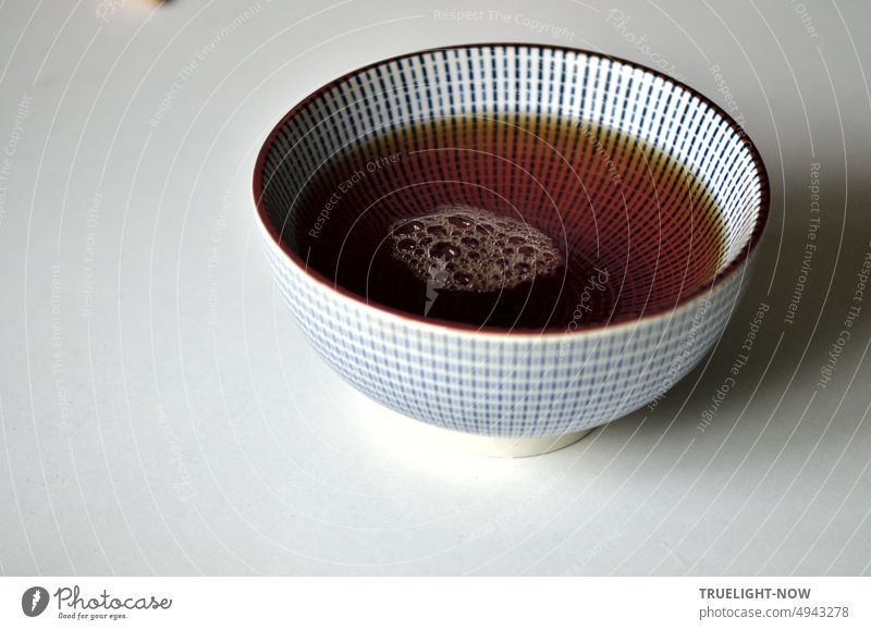 Teeschale fein blau-weiss gemustert im japanischen Tokusa Design mit frisch gebrühtem Assam Bio Schwarztee auf dem einige Luftbläschen schwimmen Keramik Japan