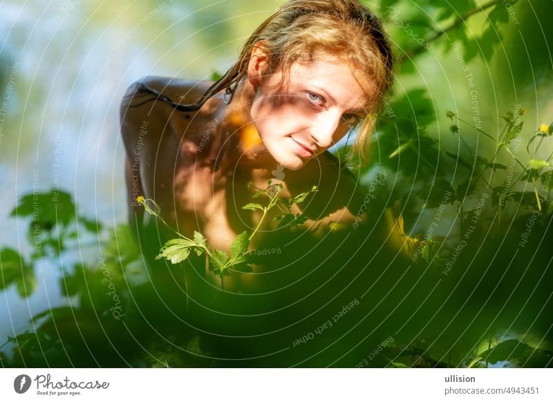 Schöne junge sexy nackte nackte Frau Mädchen, mit nassen blonden Haaren, schaut zwischen grünen gelben Blättern, an einem sonnigen Sommer See Behaarung