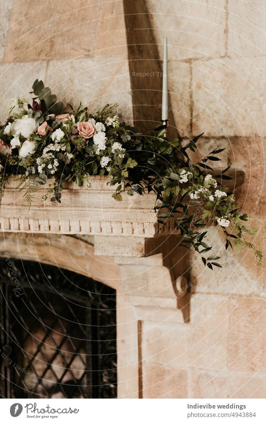 Ein schöner Blumenschmuck auf einem Kaminsturz aus Sandstein. Raum kopieren. Hochzeit Innendekoration Konzept. Weiße Rosen, Kerzen und grüne Blumen. Gusseisen Schutzgitter in den Kamin.