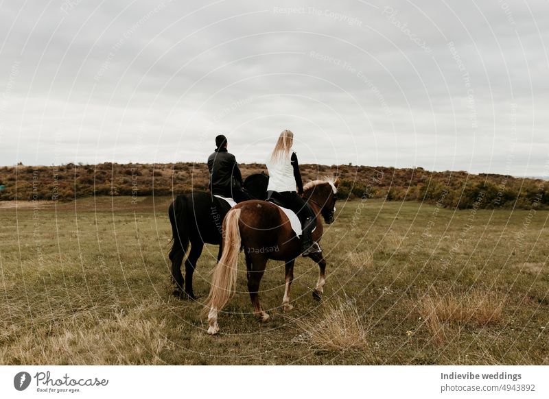 Ein Paar reitet auf einer Wiese mit Blick in die Ferne. Romantisches und aktives Date im Freien. Herbstlandschaft, mit jungen Paar genießen ein Pferd reiten. Bedecktes Wetter, schöne Pferde.