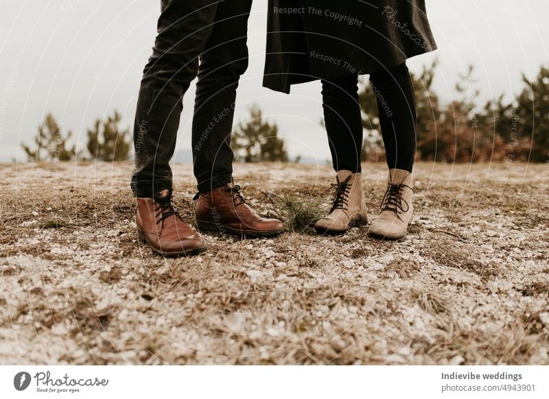 Nahaufnahme der Füße eines verliebten Paares. Herbstliches Date im Freien. Der Mann steht und trägt braune Lederstiefel, die Frau trägt beige Schuhe. Outdoor-Mode-Konzept.