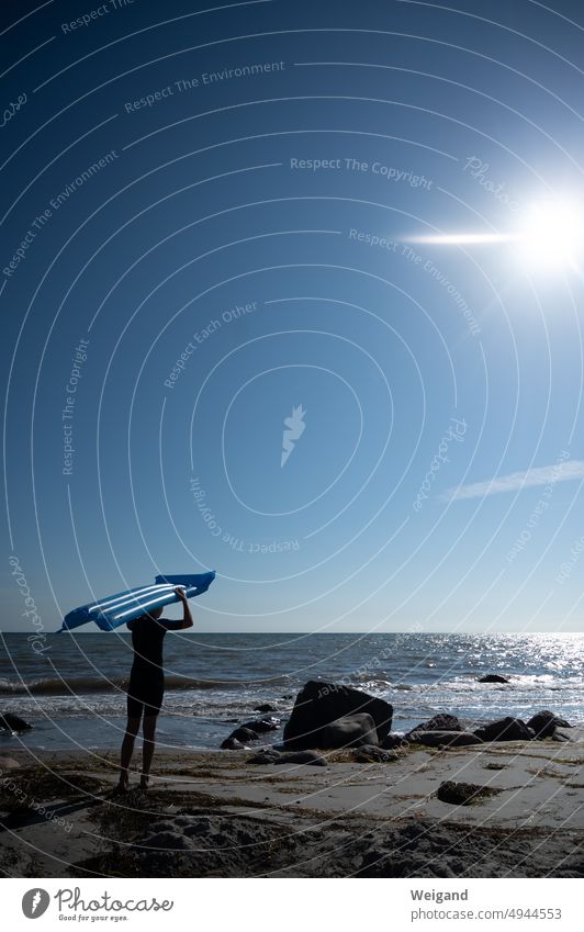 Kind mit blauer Luftmatratze am Ostsee-Strand bei Sonnenschein Sommer Felsen Urlaub Ferien Gegenlicht Nordsee Norddeutschland Schleswig-Holstein Erholung Spaß