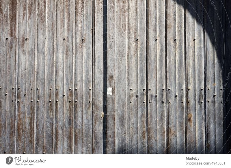 Altes graues Stahltor mit Struktur, Rost, Patina und Schatten eines Rundbogen bei Sonnenschein in den Gassen der Altstadt von Brügge in Westflandern in Belgien
