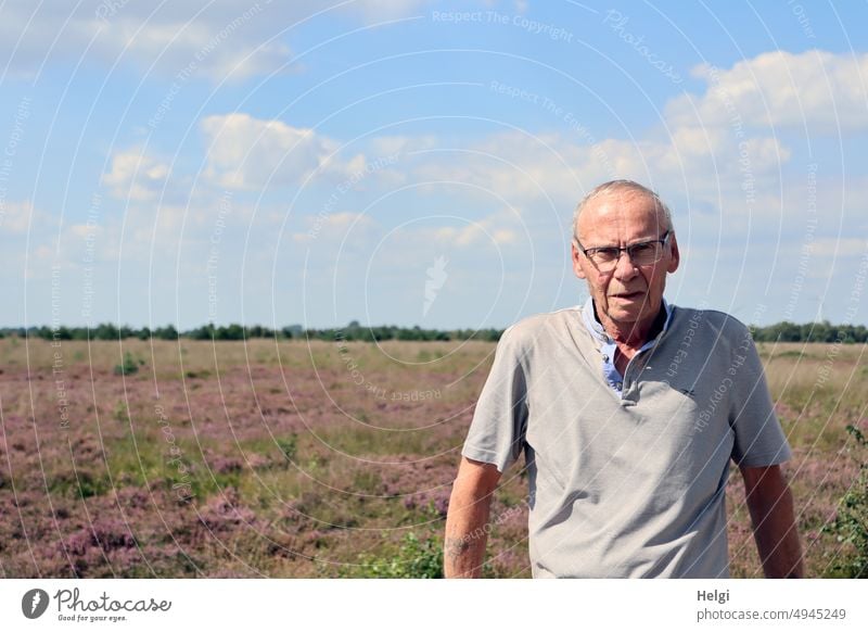 Porträt eines männlichen Senioren, im Hintergrund blühende Heidelandschaft und blauer Himmel mit Wolken Mensch Mann skeptisch Blick Sonnenschein Licht Schatten