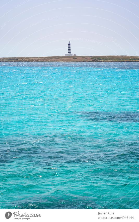 Ein türkisfarbenes Meer im Vordergrund mit einigen flachen Wellen, im Hintergrund ein blauer Leuchtturm und Schwarz, vertikal, Platz zum Kopieren Insel MEER