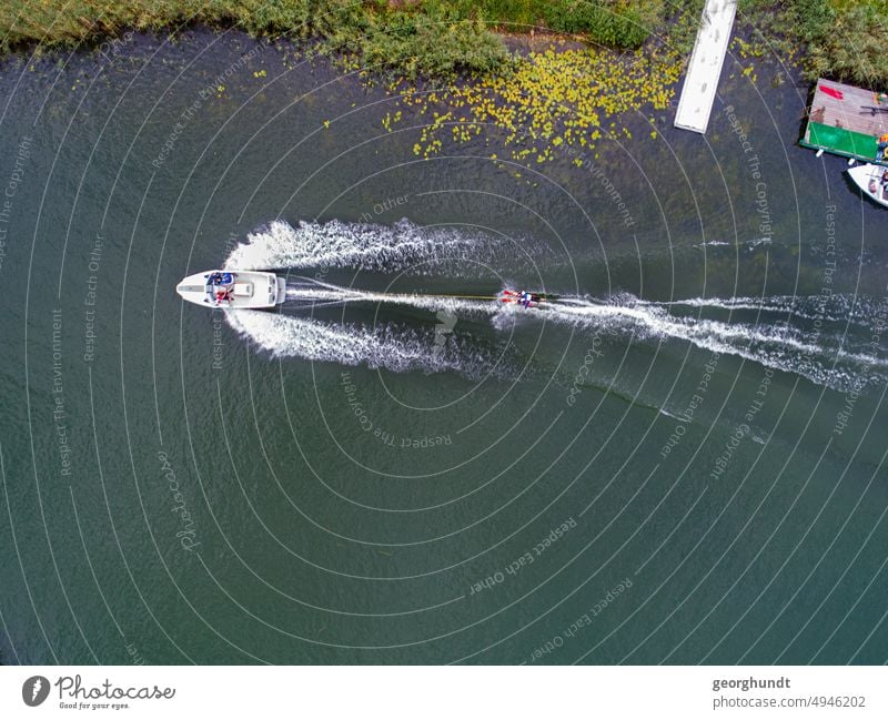 Wasserski auf einem See: Ein Motorboot zieht ein Wasserski-Sportler am Rande eines Bootsstegs Wassersport Wakeboard Binnensee Gischt Drohne Luftbild ziehen