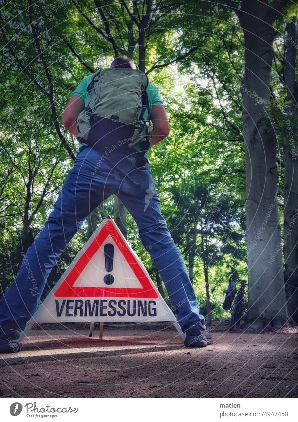 Mann bei der Vermessung Rückansicht Schild Aufsteller Park Baeume Stehen Breitbeinig Außenaufnahme