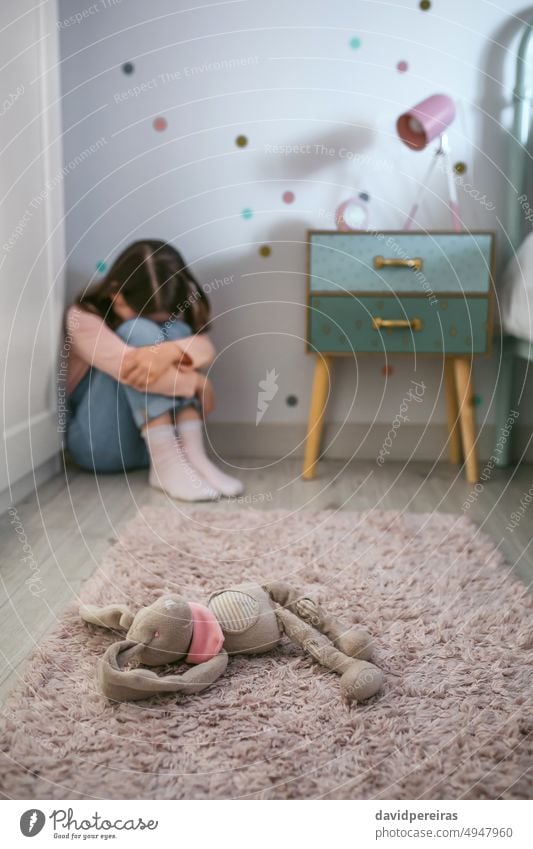 Trauriges kleines Mädchen sitzt auf dem Boden ihres Schlafzimmers und hat ein Stofftier liegen unkenntlich traurig wenig gefüllt Spielzeug Lügen Stock