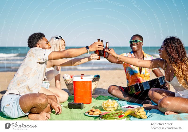 Unterschiedliche Freunde stoßen am Strand an Zuprosten Bier Picknick Lächeln Klirren Flasche Glück Wochenende Männer Frauen Sommer jung vielfältig