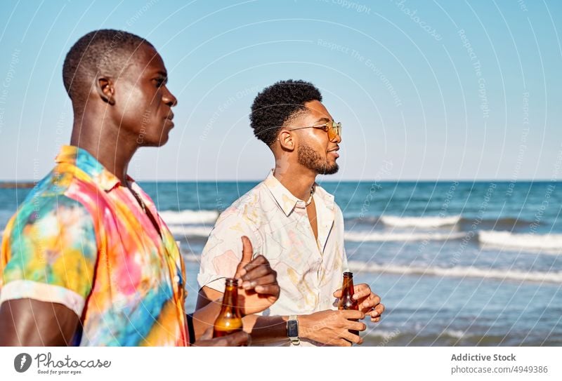 Zufriedene schwarze Männer mit Bierflaschen, die das Meer bewundern Strand Freund Talkrunde Zusammensein trinken Urlaub Sommer Feiertag Zeit verbringen jung