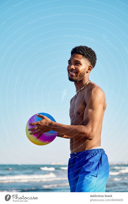 Fröhliches schwarzes Männchen mit Ball am Meer Mann Lächeln Strand Wochenende MEER Blauer Himmel Urlaub Sommer Glück männlich Afroamerikaner ethnisch heiter