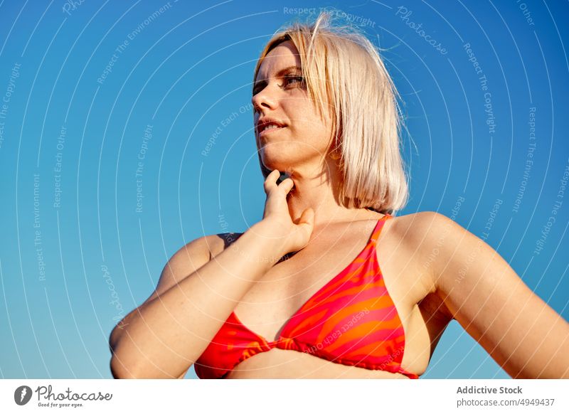 Weiblicher Tourist am Meer stehend Frau MEER Strand Sommer Tasthals Wochenende Urlaub Resort winken jung Hand auf der Taille blond Bikini Ufer Küste Wasser