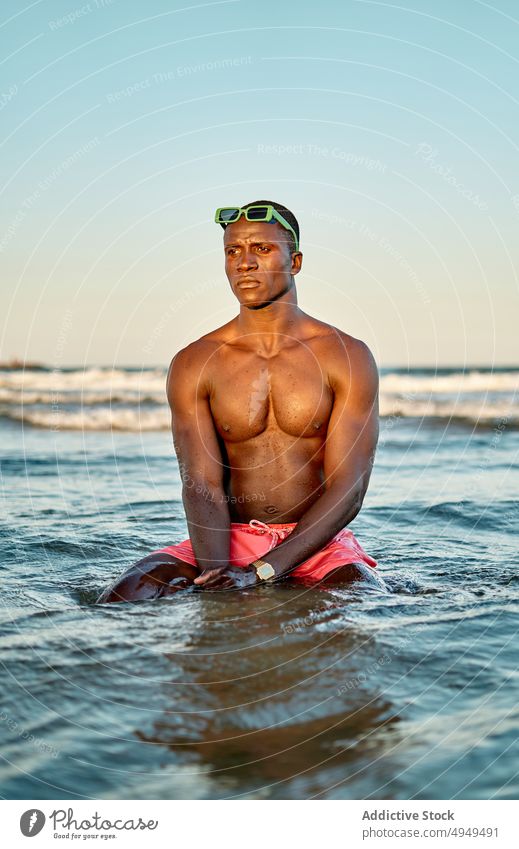 Nachdenklicher schwarzer Mann ohne Hemd im Meerwasser MEER Wasser Wochenende Sommer ausrichten Sonnenbrille Urlaub Sauberkeit männlich muskulös jung