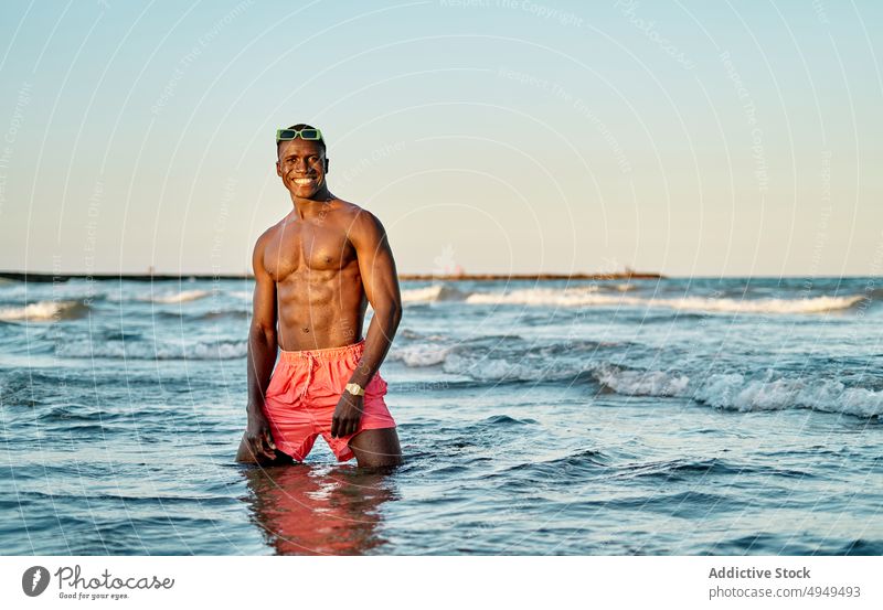 Hemdloser lächelnder schwarzer Mann im Meerwasser MEER Wasser Wochenende Sommer ausrichten Sonnenbrille ohne Hemd Urlaub Sauberkeit stehen männlich muskulös