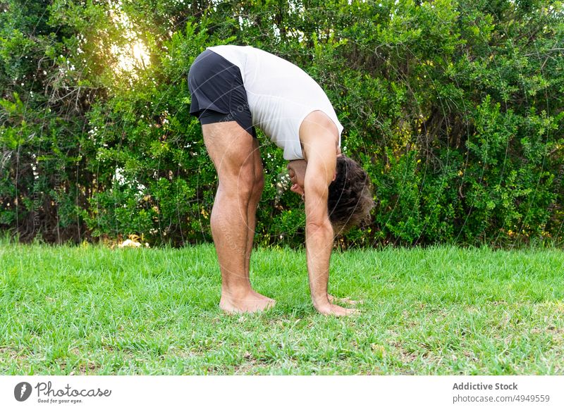 Flexibler Mann macht Standing Forward Bend im Park Yoga Sitzung Gras berühren stehende Vorwärtsbeuge Dehnung üben beweglich Buchse männlich Barfuß Rasen