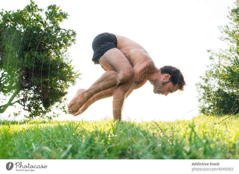 Älterer Mann macht Crow Pose auf Gras Yoga Gleichgewicht üben Sommer Rasen Krähenstellung Asana Barfuß männlich Wohlbefinden Dehnung Energie Zen friedlich