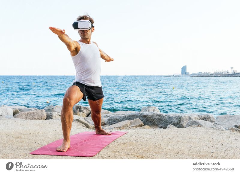Mann mit VR-Brille in Krieger-Pose Yoga Sitzung Strand MEER Headset üben Gleichgewicht männlich Backend Arm angehoben Zen Ufer Wohlbefinden Wellness