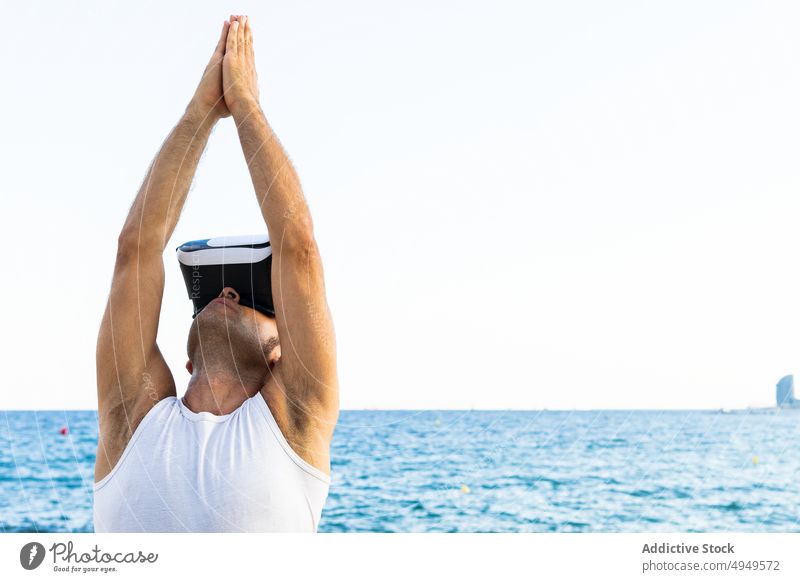 Mann mit VR-Brille streckt sich am Meer Dehnung Schutzhelm MEER Yoga Sitzung Arme hochgezogen üben Zen männlich reif Lebensmitte Aktivität Hobby Wellness