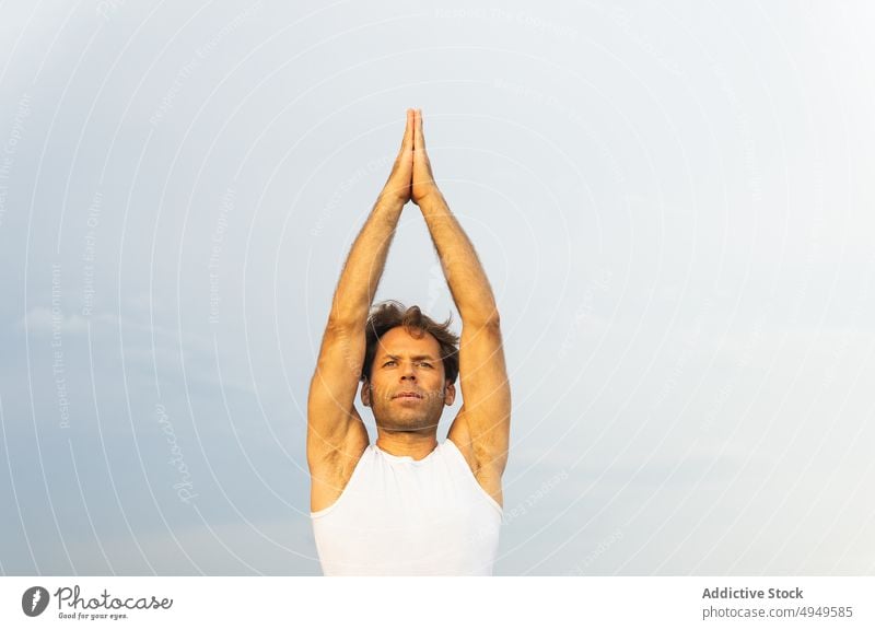 Älterer Mann macht Vriksasana Pose gegen grauen Himmel Yoga üben Gleichgewicht Baumhaltung Sommer Zen männlich tagsüber Wohlbefinden Energie Arme hochgezogen