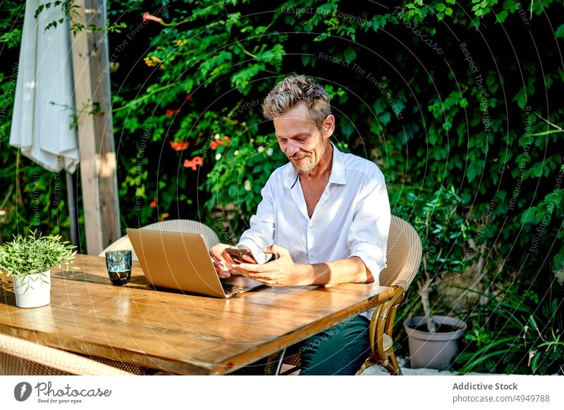 Älterer Manager benutzt Smartphone im Restaurant Geschäftsmann benutzend Telearbeit Lächeln Pause Tisch Laptop Daten männlich reif Lebensmitte Projekt