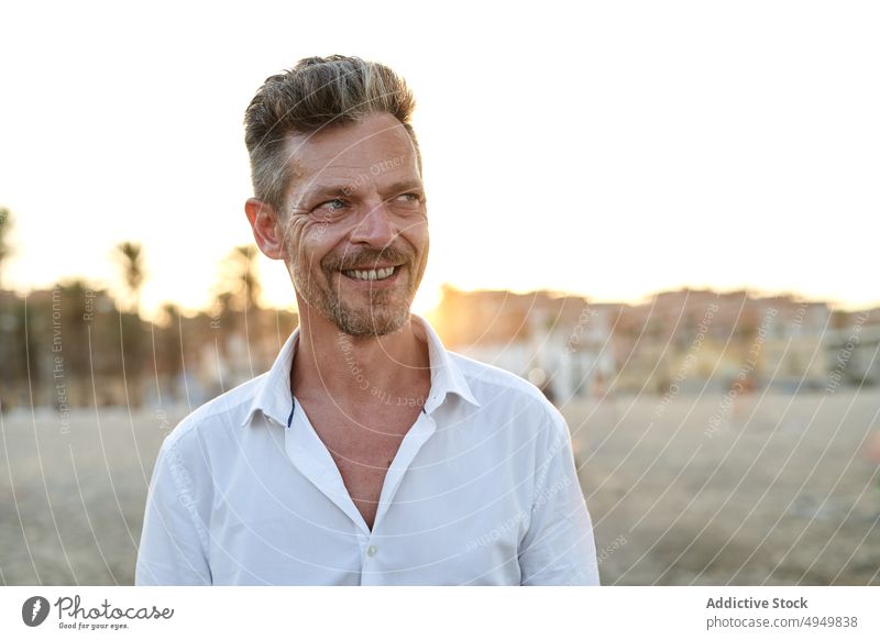 Glücklicher reifer Mann am Strand bei Sonnenuntergang Lächeln Urlaub Sommer Wochenende Resort Porträt männlich heiter Lebensmitte positiv froh Inhalt sorgenfrei