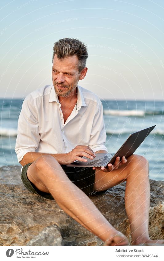 Älterer Geschäftsmann bei der Arbeit auf den Felsen am Meer Laptop benutzend MEER Lächeln Daten Telearbeit männlich reif Lebensmitte unabhängig Projekt