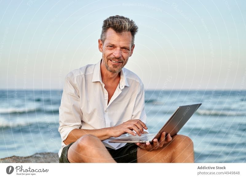 Älterer Geschäftsmann bei der Arbeit auf den Felsen am Meer Laptop benutzend MEER Lächeln Daten Telearbeit männlich reif Lebensmitte unabhängig Projekt