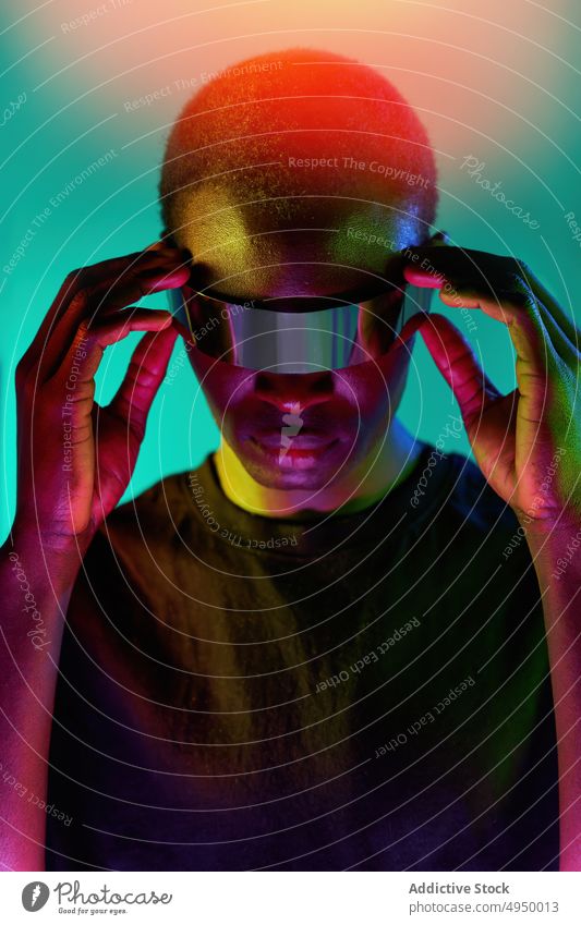 Ernster junger ethnischer Mann berührt VR-Brille in Neon-Studio Virtuelle Realität erkunden futuristisch eintauchen cool digital Erfahrung ausrichten