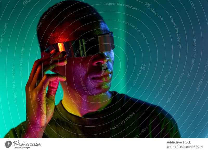Ernster junger ethnischer Mann berührt VR-Brille in Neon-Studio Virtuelle Realität erkunden futuristisch eintauchen cool digital Erfahrung ausrichten
