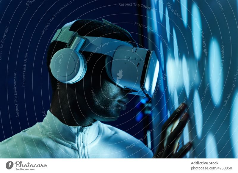 Ernster schwarzer Mann, der einen großen Bildschirm berührt, während er die virtuelle Realität mit einem modernen Headset erkundet Virtuelle Realität