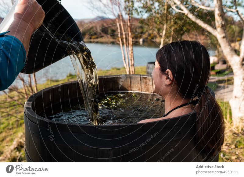 Mann gießt heißes Wasser für Frau in Fass eingießen Bad See Ufer Algen Spa ruhen Tourist Herbst Erholung Teich Eimer Landschaft Becken Saison Dienst Waschen