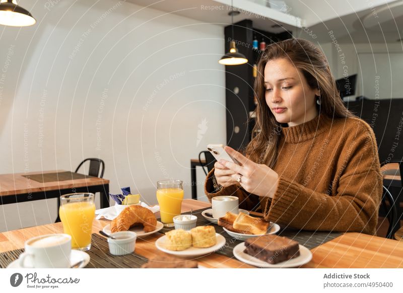 Frau benutzt Smartphone beim Frühstück in der Cafeteria Nachricht Getränk Café soziale Netzwerke benutzend Talkrunde Zuprosten Pullover Handy Browsen Kaffee