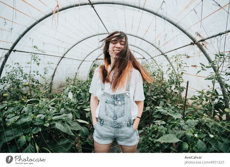 Junge Frau mit wehenden Haaren im Gewächshaus bei Pflanzen mit Gemüse. Nachhaltigkeit und verantwortungsvoller Anbau Konzept. Öko und Bio gesunde Lebensmittel Ernte.