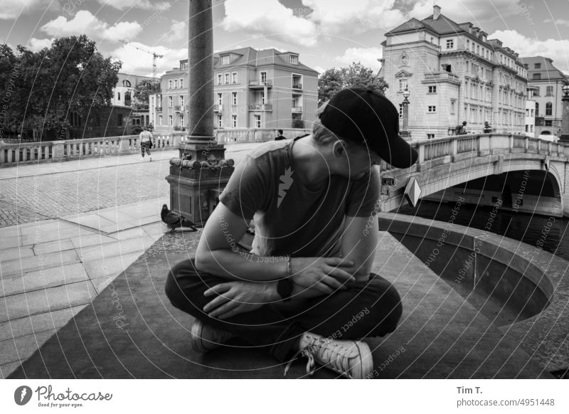 ein junger Mann mit Cap blickt sitzend nach unten Berlin Mitte Spree Brücke s/w Baseballmütze bnw Außenaufnahme Tag Schwarzweißfoto Hauptstadt Stadtzentrum