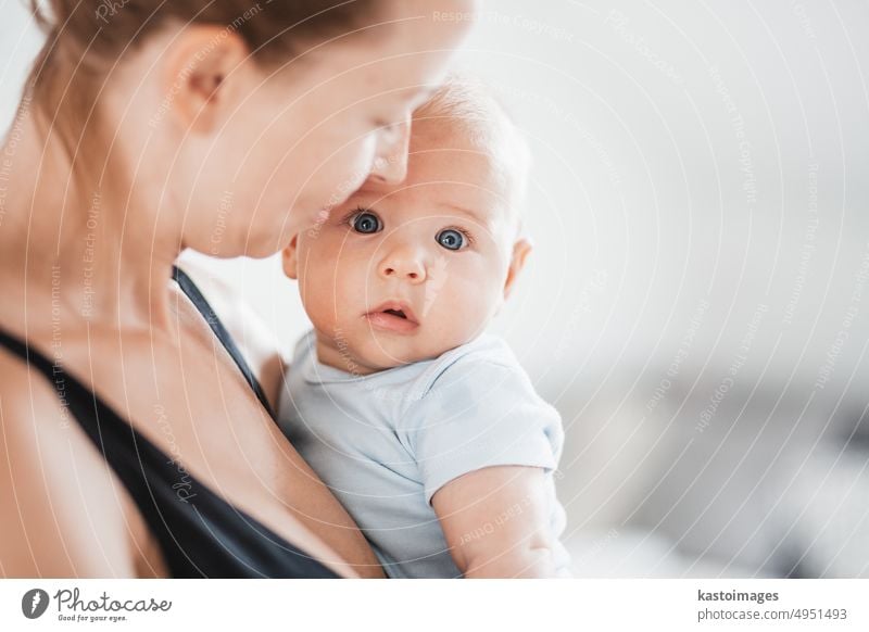 Porträt eines süßen Babys, das in den Armen seiner Mutter ruht und in die Kamera schaut. Neue Mutter hält und kuscheln kleines Kind, umarmt Kind mit Zärtlichkeit, Liebe, Pflege. Mutterschaft Konzept.