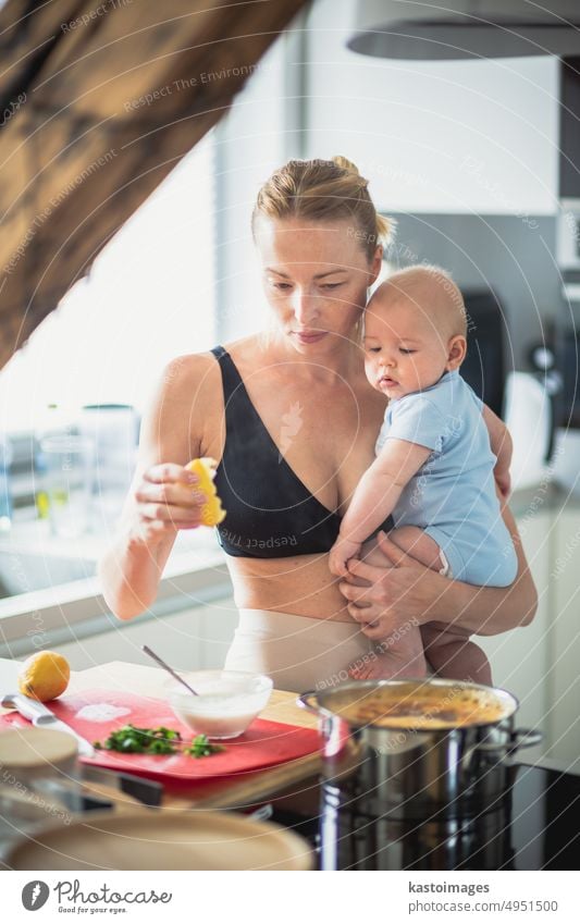 Eine Frau kocht, während sie ein vier Monate altes Baby in den Händen hält. Kindheit Familie Mutterschaft Eltern Küche heimwärts Sohn Junge beschäftigt