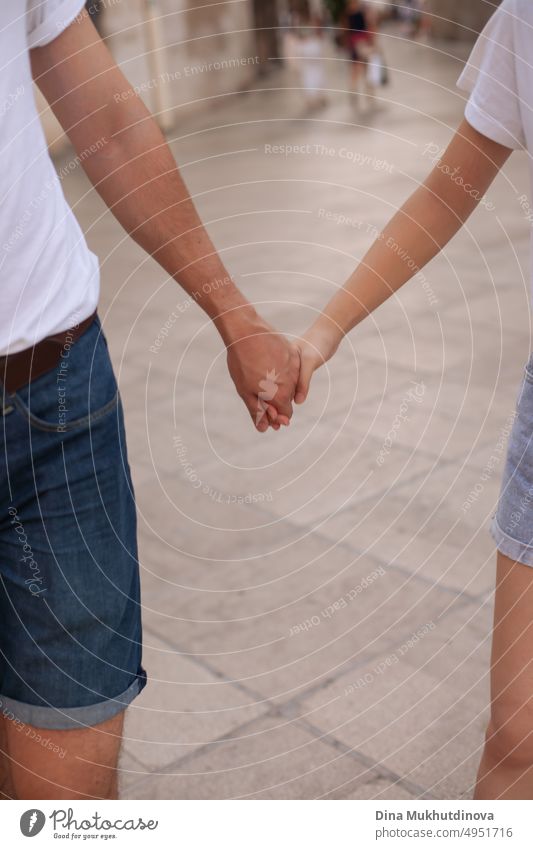 Ein gemischtrassiges Paar hält sich an den Händen. Unterschiedliche Menschen halten sich bei einem Spaziergang in der Stadt an den Händen. Liebe und Freundschaft. Bindung. Zusammenhalten. Junger Mann und Mädchen halten sich an den Händen.