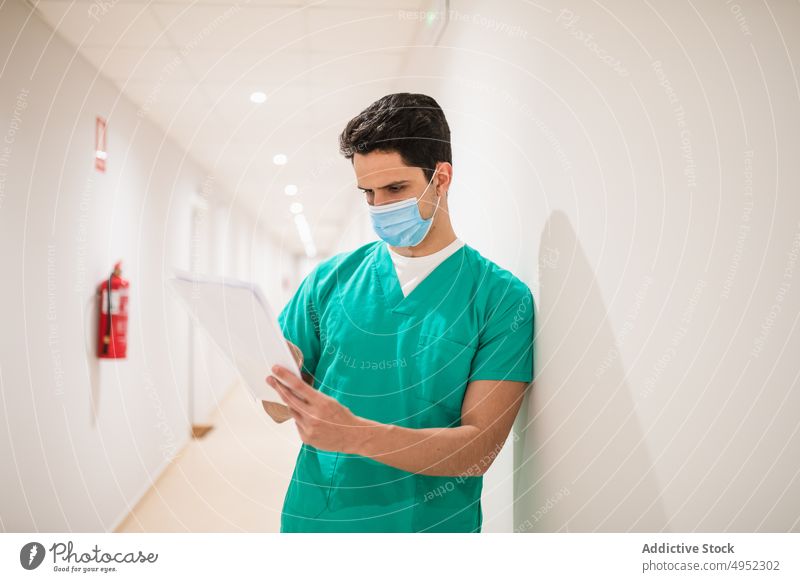 Aufmerksamer Arzt mit Papieren auf dem Krankenhausflur lesen Uniform professionell Job steril achtsam Mann Gang Chirurg Licht Lampe glänzend Fokus Sanitäter